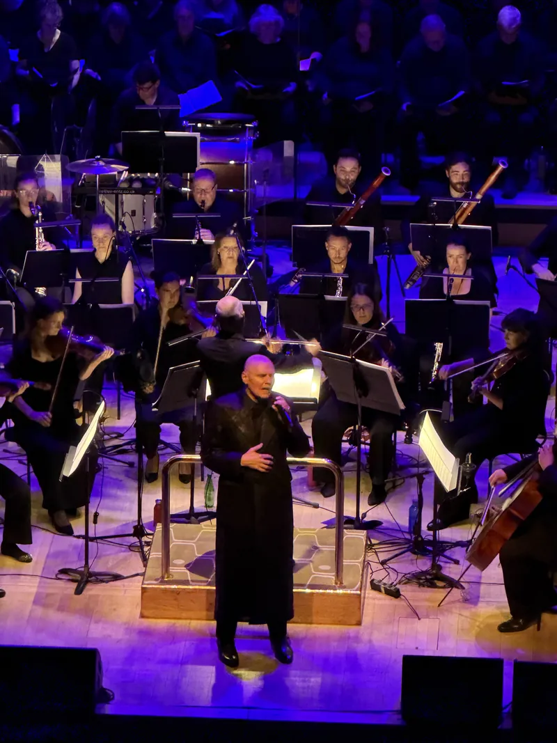Billy Corgan singing at the podium microphone, framed by the orchestra's string and woodwind sections under warm stage lighting.