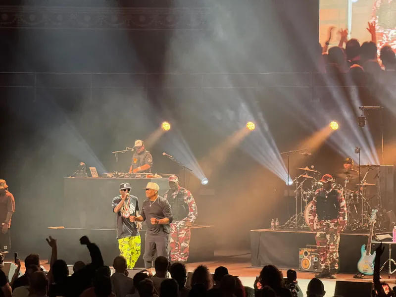 Flava Flav and Chuck D on stage. There are men standing either side of them at attention.