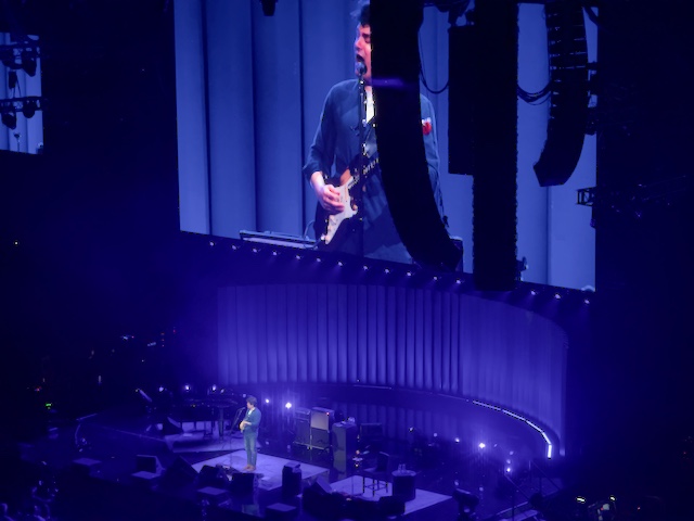 John standing center stage playing his signature Fender Stratocaster guitar and singing