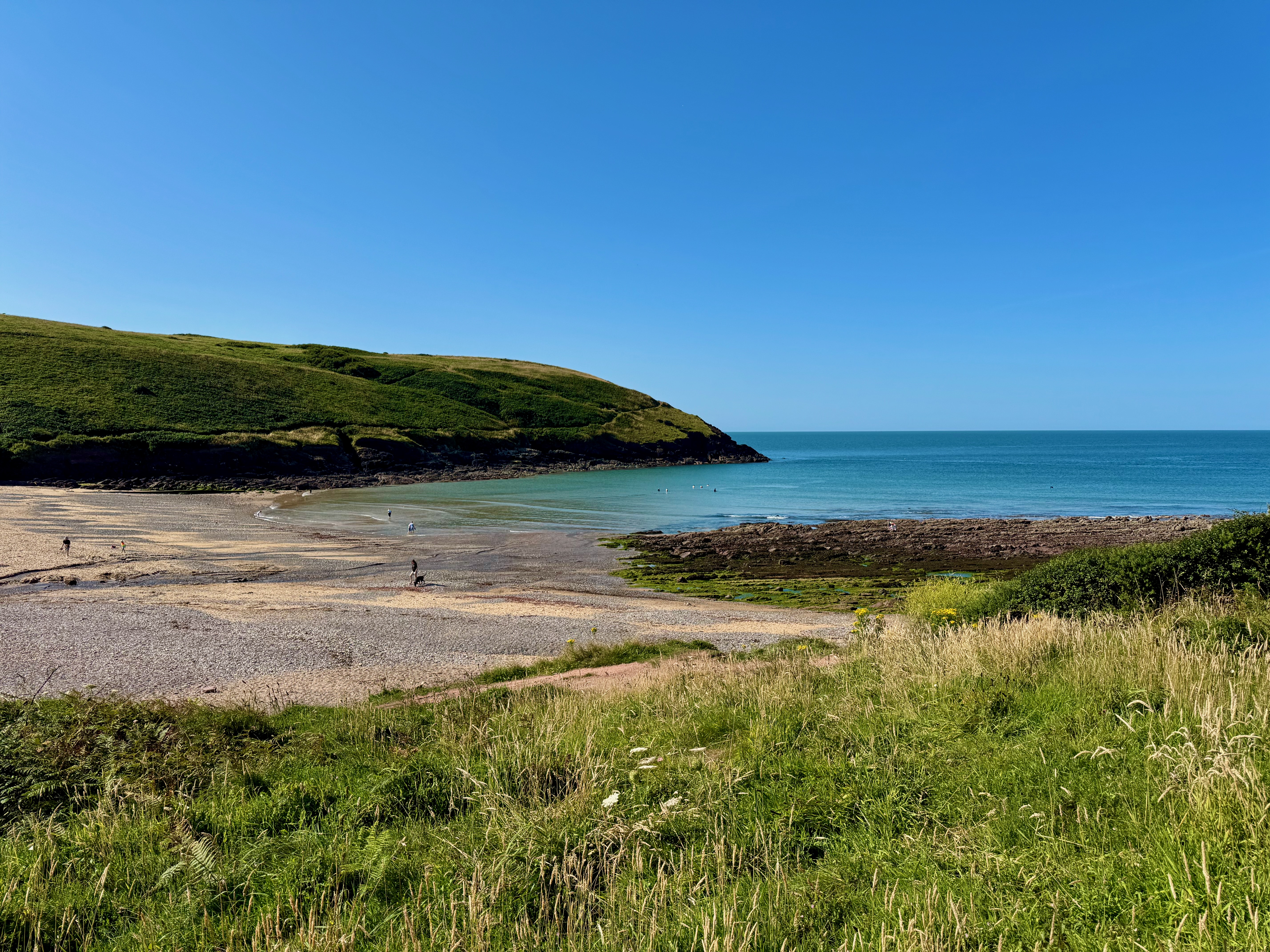 Manorbier Beach on the left with the bay on the right. Some people wondering along the beach