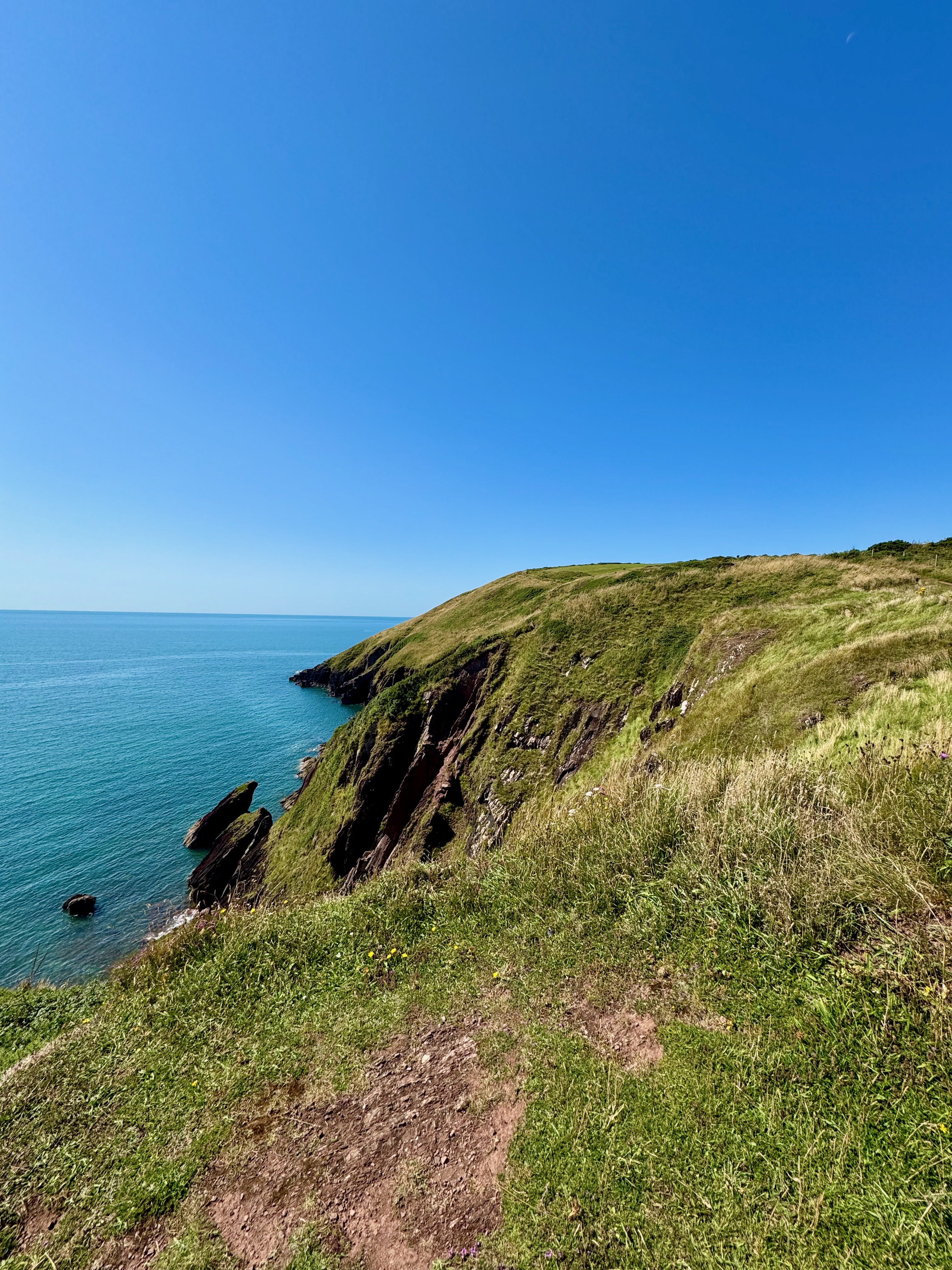 The trail running across the top of a cliff that drops off to the left down into the sea of bright blue water