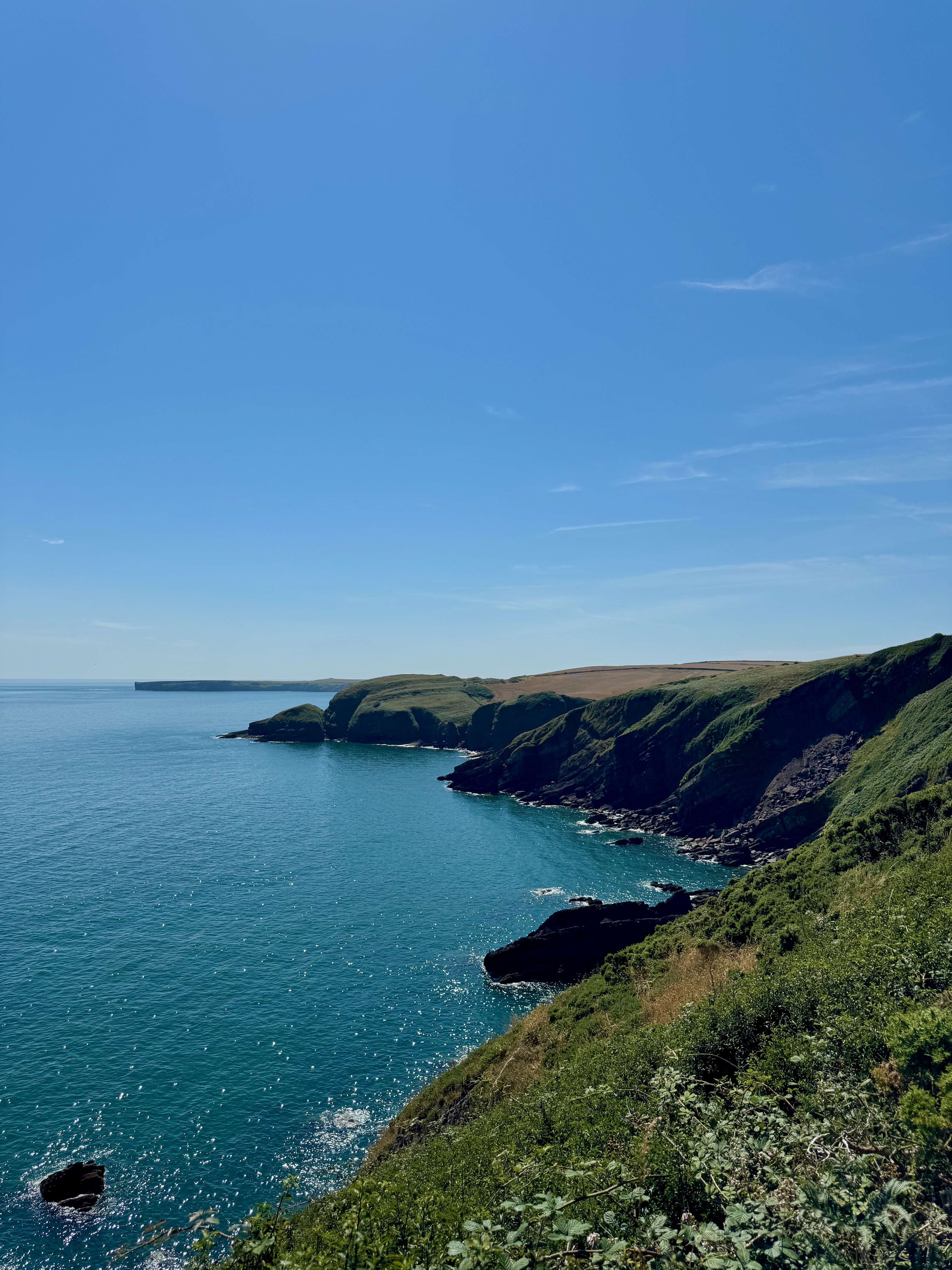 On top of a cliff that drops off to the left down into the sea of bright blue water.