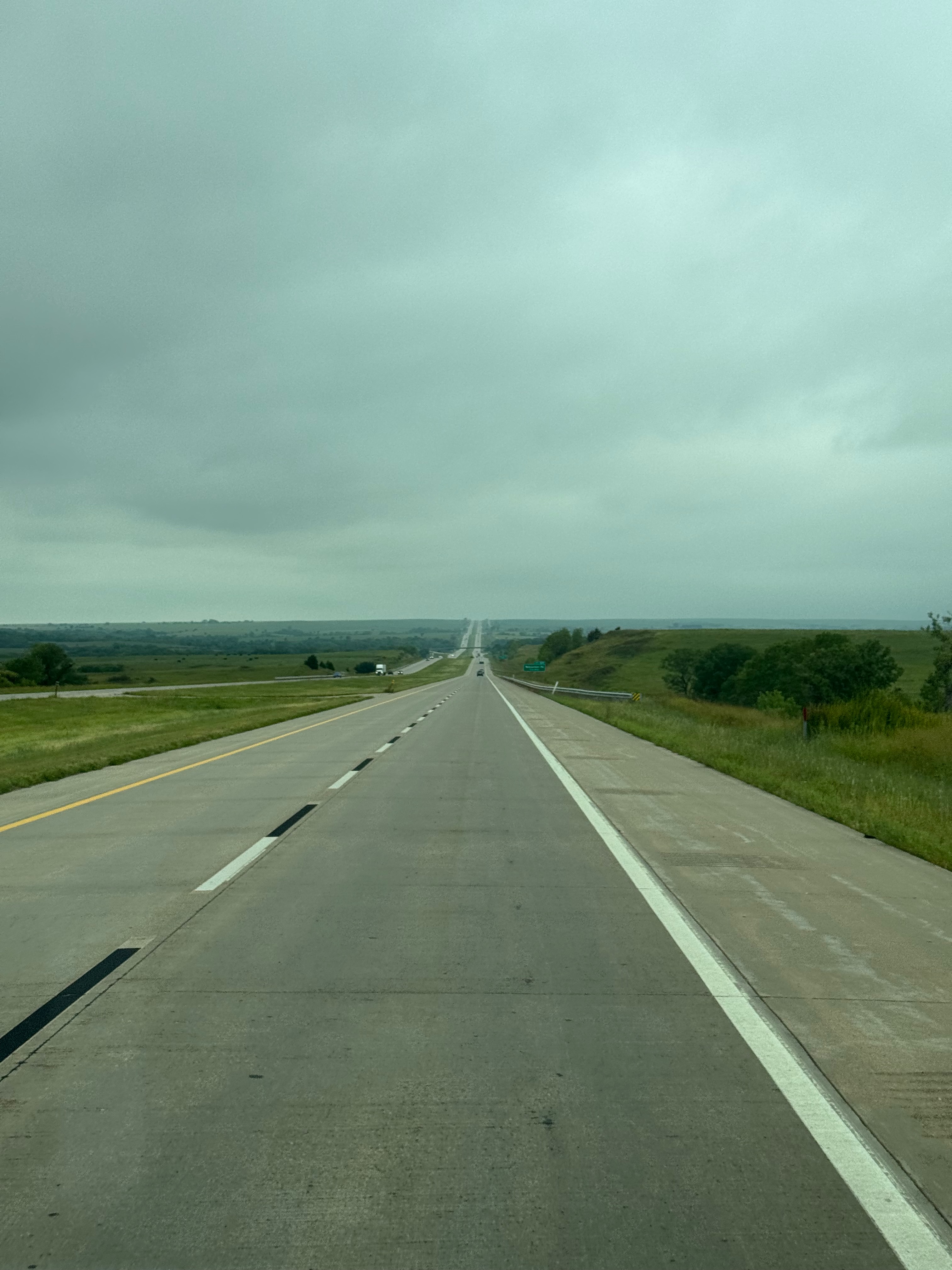 Looking straight down a long interstate road with rolling hills and clouds over head.