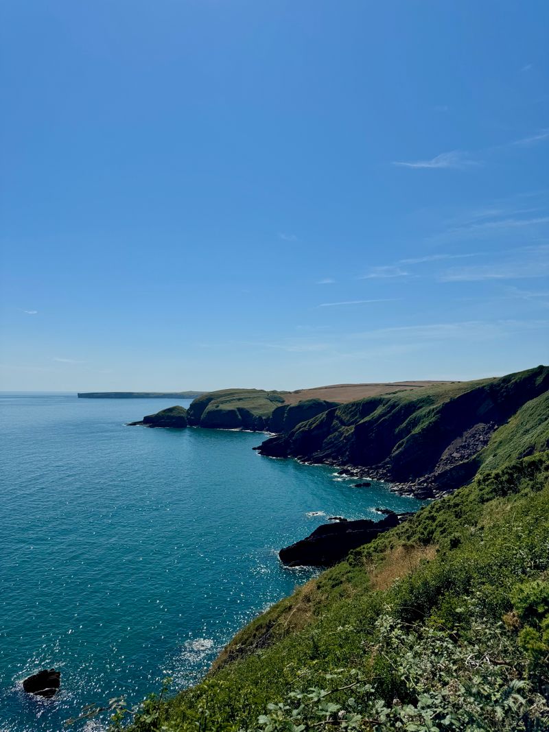 On top of a cliff that drops off to the left down into the sea of bright blue water.