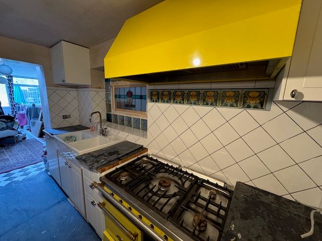 kitchen with yellow stove white tiles on the wall and white cabinets. There are still unfinished bits like no paint on the ceiling and no electrical sockets hooked up yet.