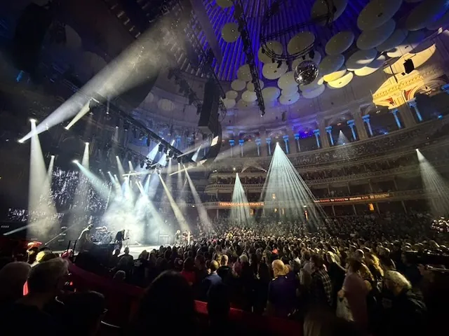 Panoramic view of the Royal Albert Hall during the Garbage concert, with powerful white beams of light shooting from the stage through the haze over a packed standing crowd. The hall's distinctive acoustic dishes hang from the ceiling.