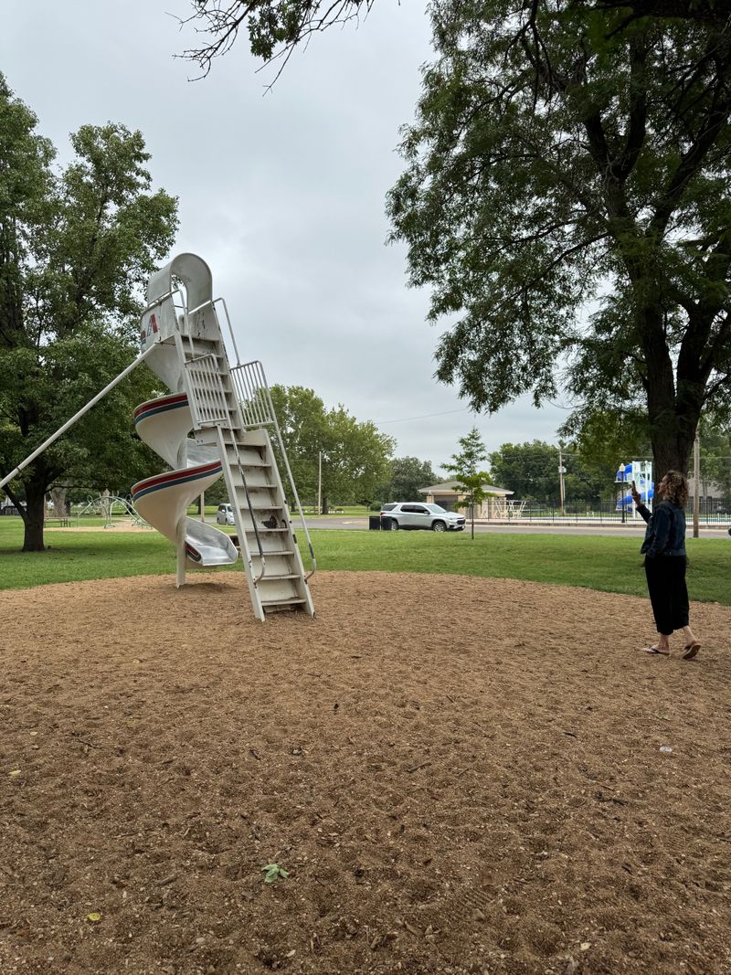 In the middle of a course sandpit surrounded by green grass is a tall twirling slide