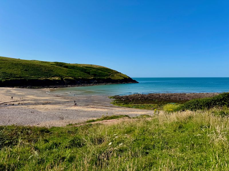 Manorbier Beach on the left with the bay on the right. Some people wondering along the beach