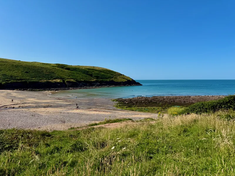 Manorbier Beach on the left with the bay on the right. Some people wondering along the beach