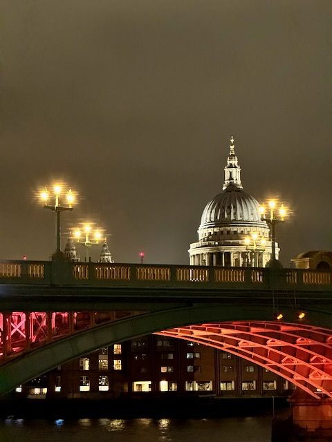 Southwark Bridge all lit up at night with the top of St. Paul's showing behind it.