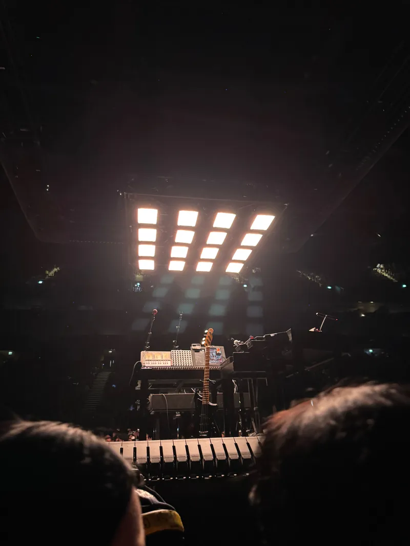 A 4 by 4 grid of white lights shine down on the small stage. There's a bass guitar and some keyboards on the stage.