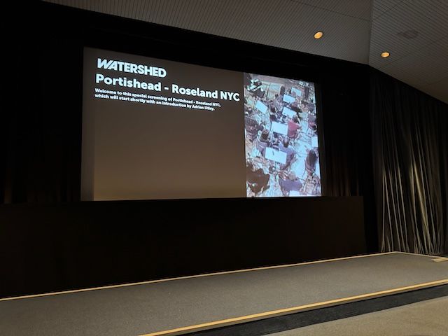 View of cinema screen from the second row. Text saying Portishead - Roseland NYC on the screen.