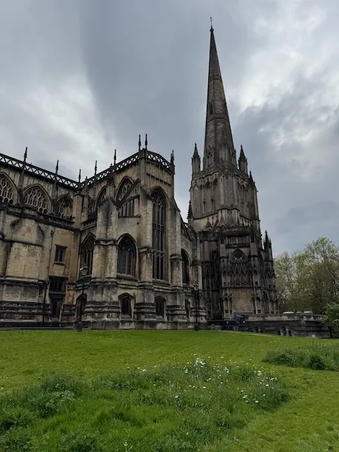 A wide angle shot of an old cathedral in Bristol with grey skies in the background and green grass in the foreground